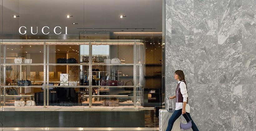 Woman walking past a Gucci store carrying shopping bags inside a busy shopping centre
