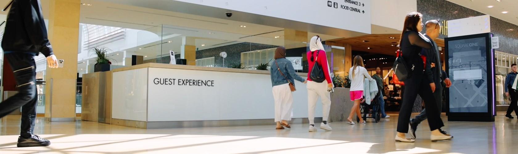 Shoppers walking past a guest experience desk and digital directory screen inside the shopping Mall