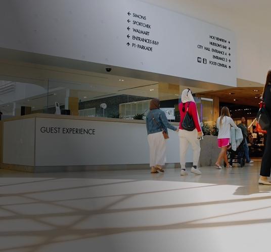 Shoppers walking past a guest experience desk and directory signage inside the shopping centre