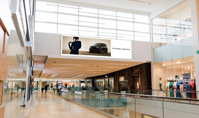 Shopping centre interior featuring digital screens with shoppers viewing media content